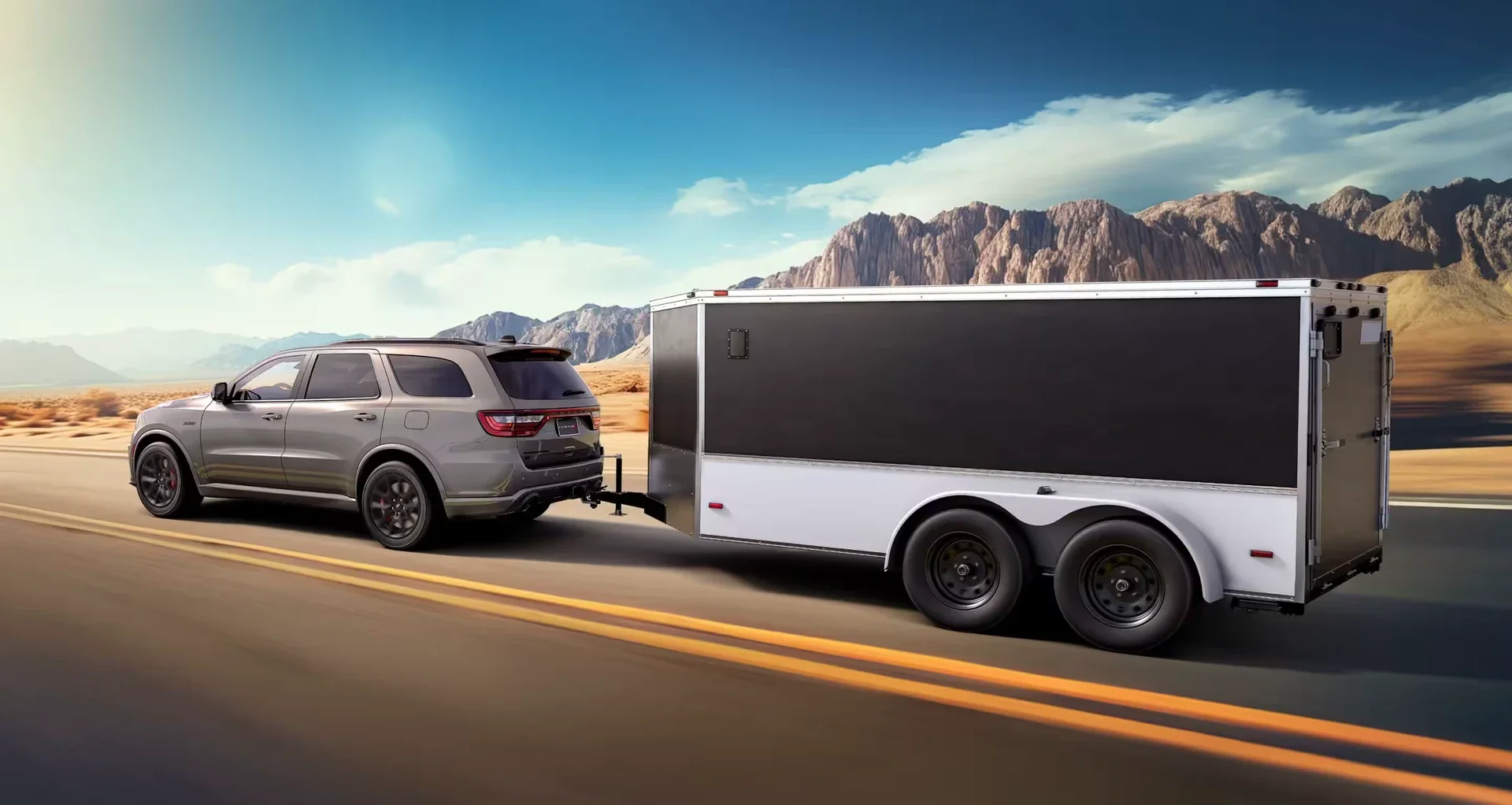 A silver Dodge Durango towing an enclosed trailer on a desert highway.