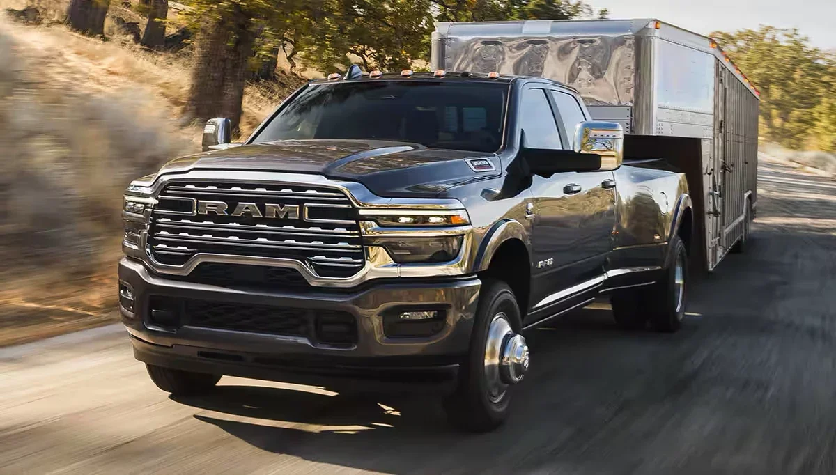 A 2026 Ram 3500 dually towing a silver travel trailer on a dusty road.