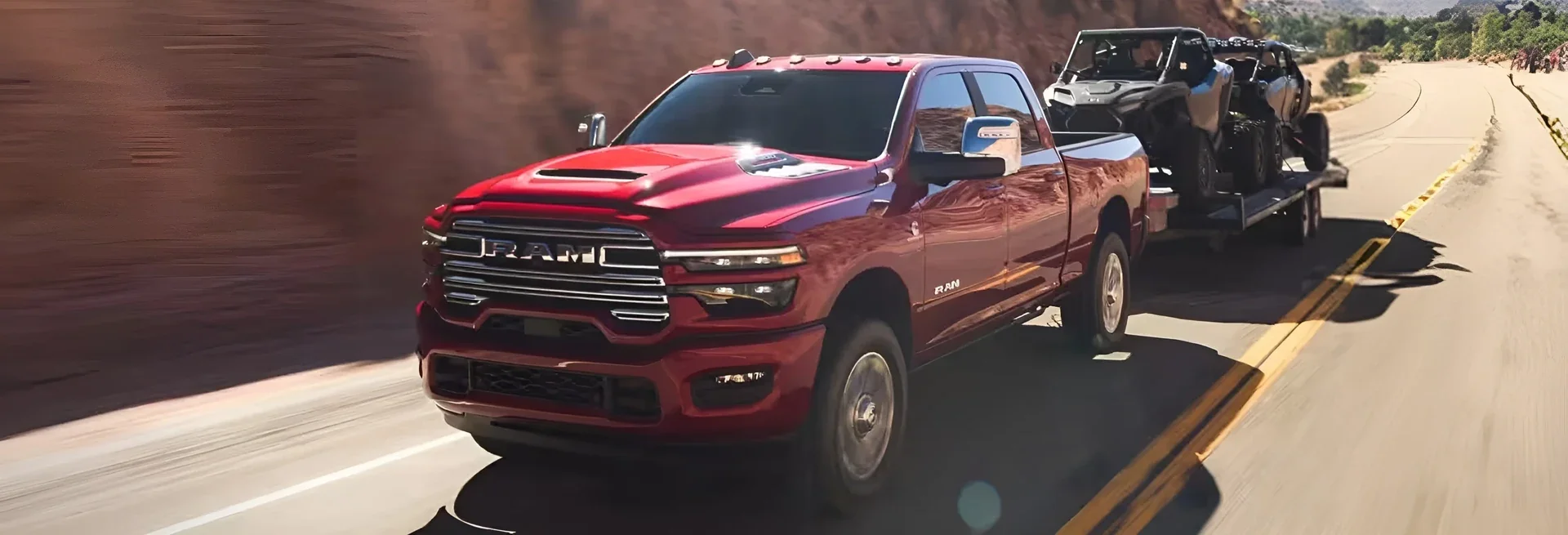 A red Ram towing an off-road vehicle on a trailer down the highway.