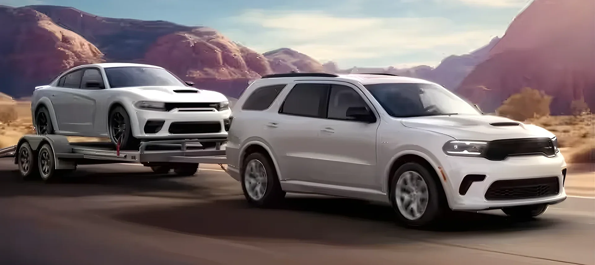 A white Dodge Durango towing a white Charger on a car trailer.