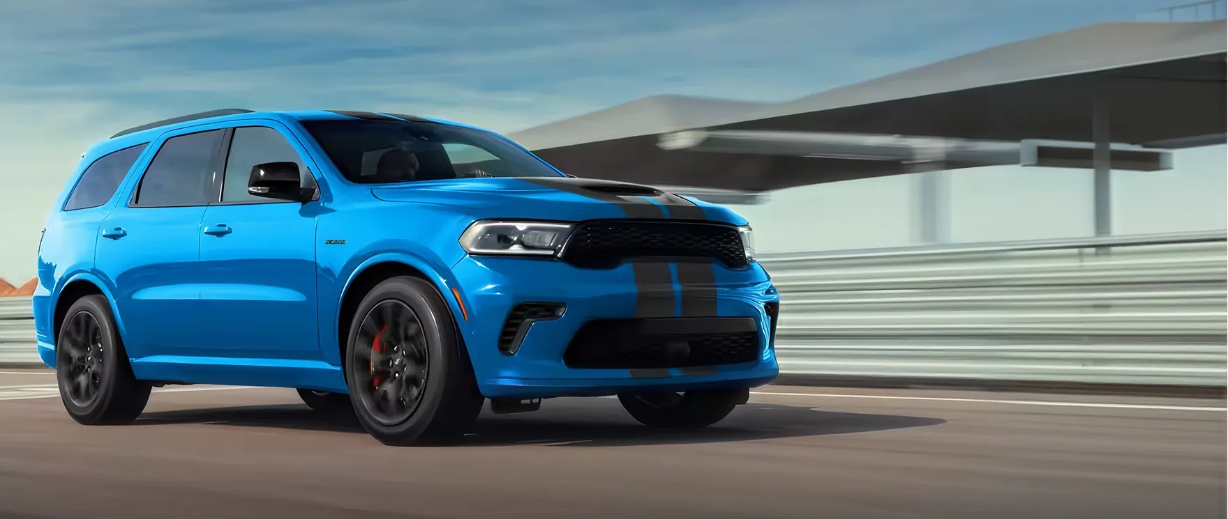Blue Dodge Durango with black stripes driving past a glass facade