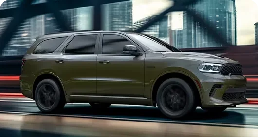 Olive Dodge Durango driving past a city skyline at dusk