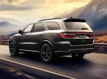 Dark Dodge Durango driving at sunset, rear three-quarter view