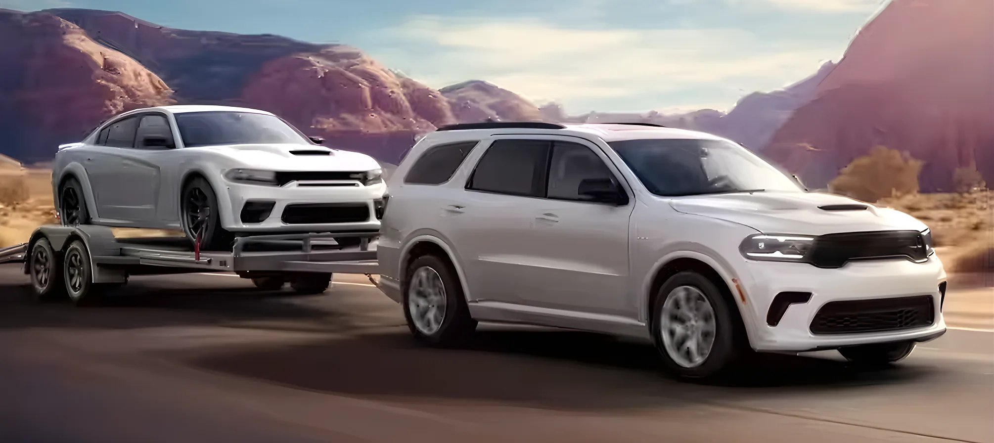 White Dodge Durango towing a white Dodge Charger on a trailer through red rock country