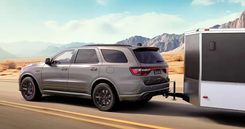 Grey Dodge Durango towing a white trailer along a mountain highway
