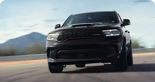 Black Dodge Durango head-on on a coastal road with mountains behind