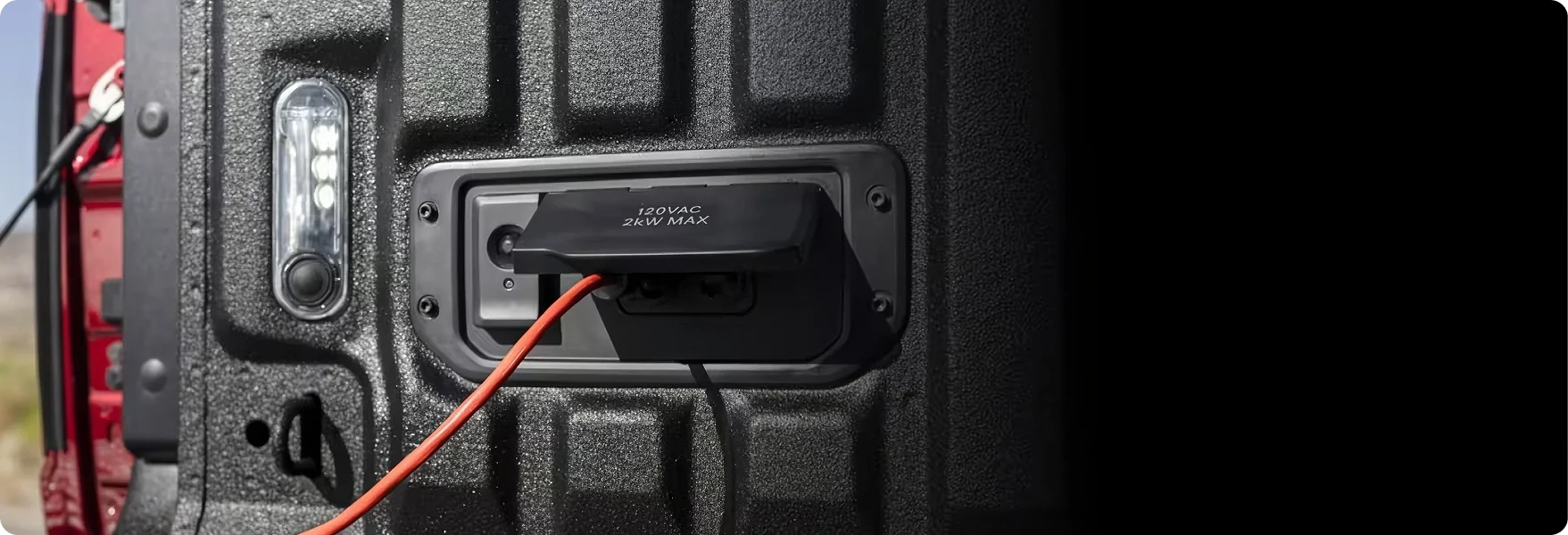 Extension cord plugged into the 120-volt outlet inside the bed of a red RAM 1500