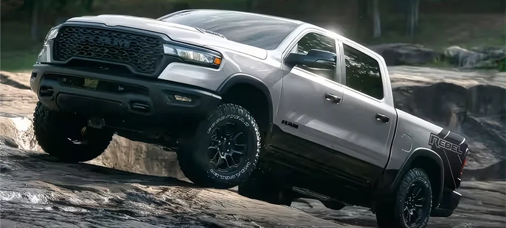 Silver RAM 1500 Rebel angled over a rock ledge on a wooded trail