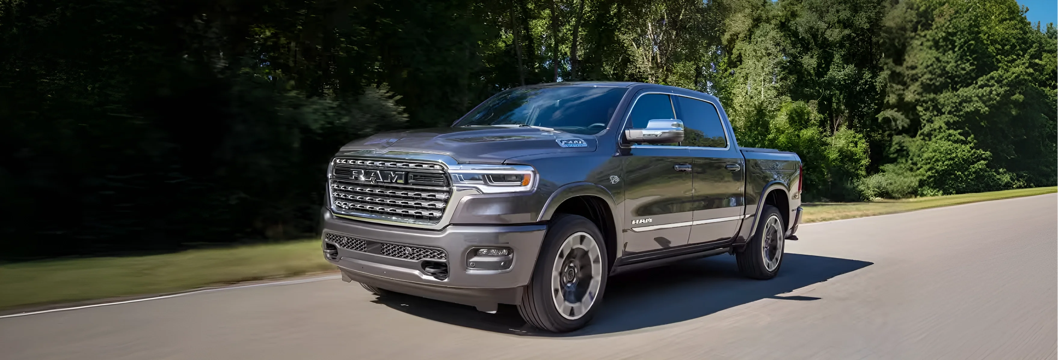 Gray RAM 1500 Limited driving on a paved road beside a dense treeline
