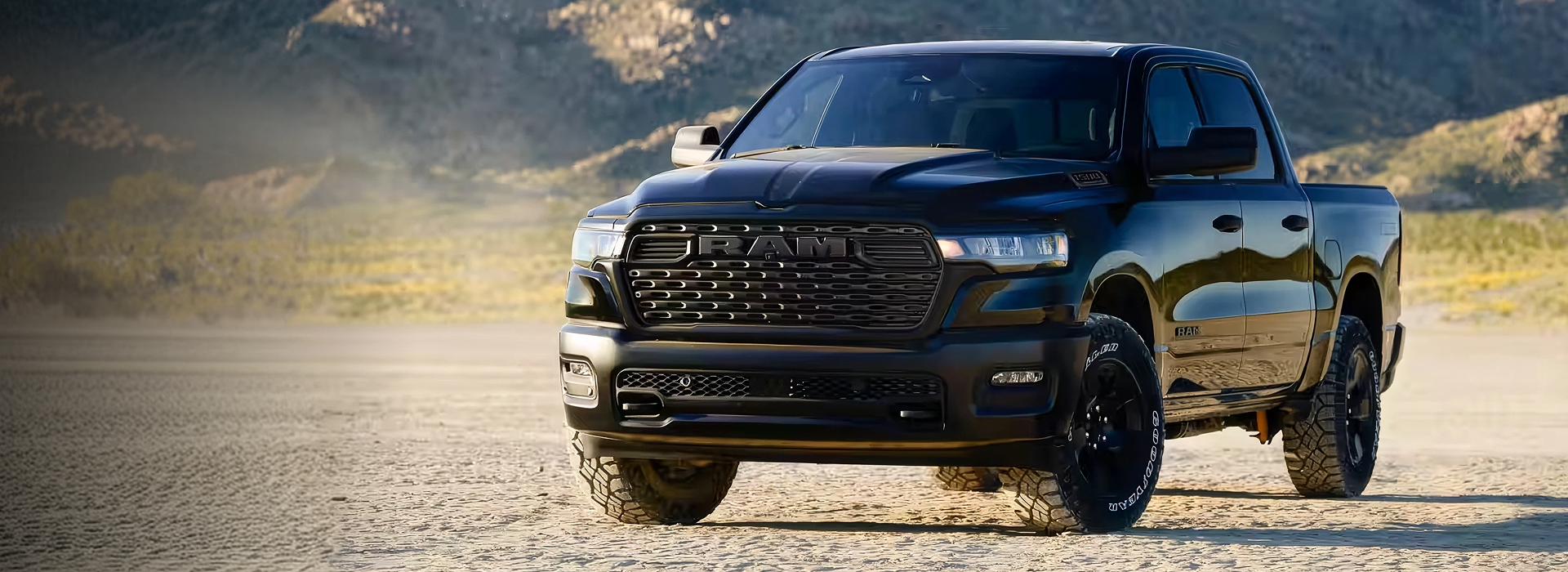 Black 2026 RAM 1500 crew cab pickup parked on a dry desert flat with rocky hills behind it