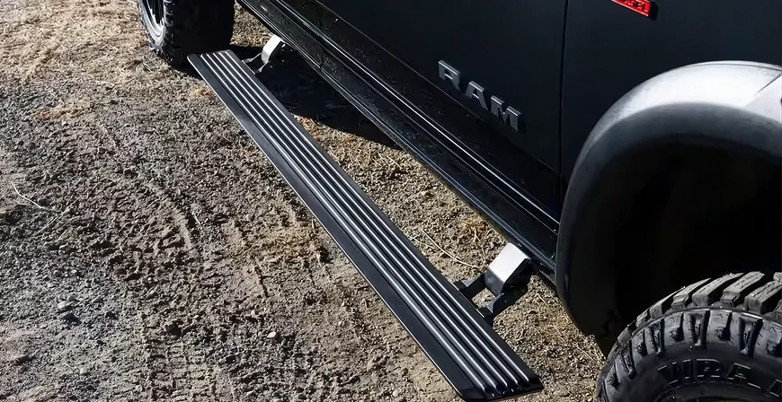 Deployed power side running board along the rocker panel of a black RAM 2500 on gravel