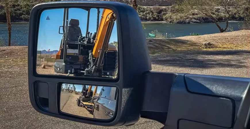 Extended power convex trailer tow mirror on a RAM 2500 reflecting a yellow excavator on a trailer