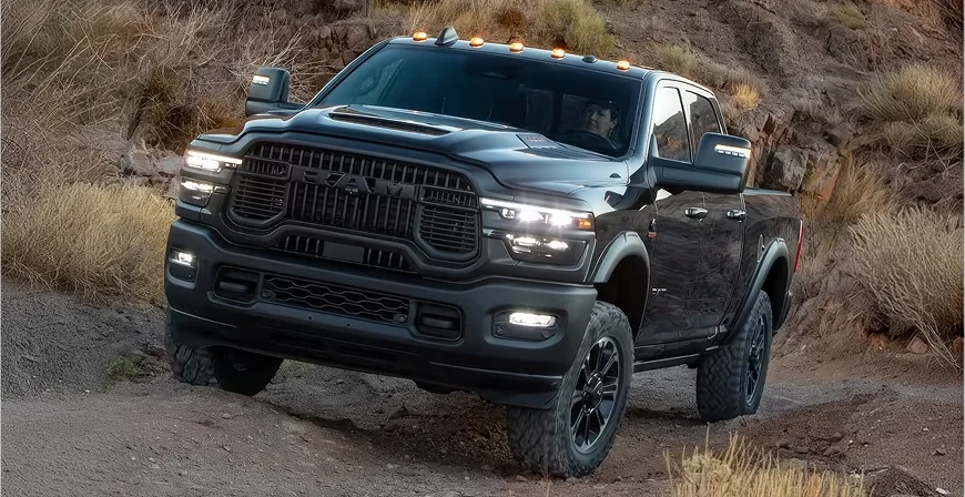 Dark green RAM 2500 climbing a rocky slope with its LED headlamps and fog lamps lit