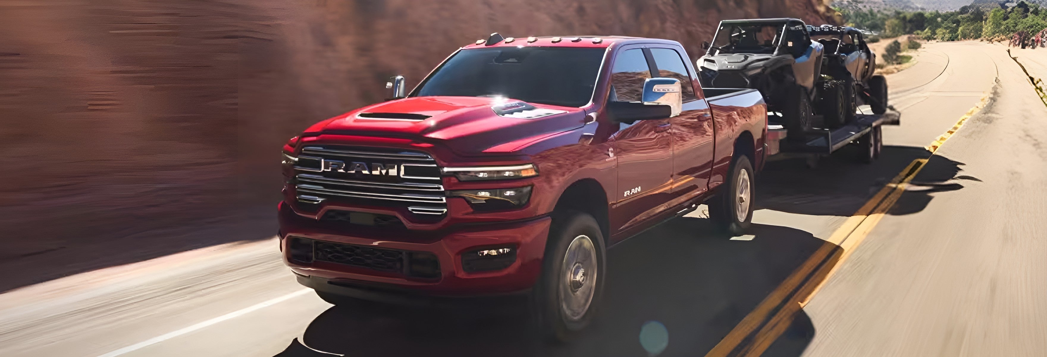 Red RAM 2500 towing a trailer loaded with two side-by-sides along a curving canyon road