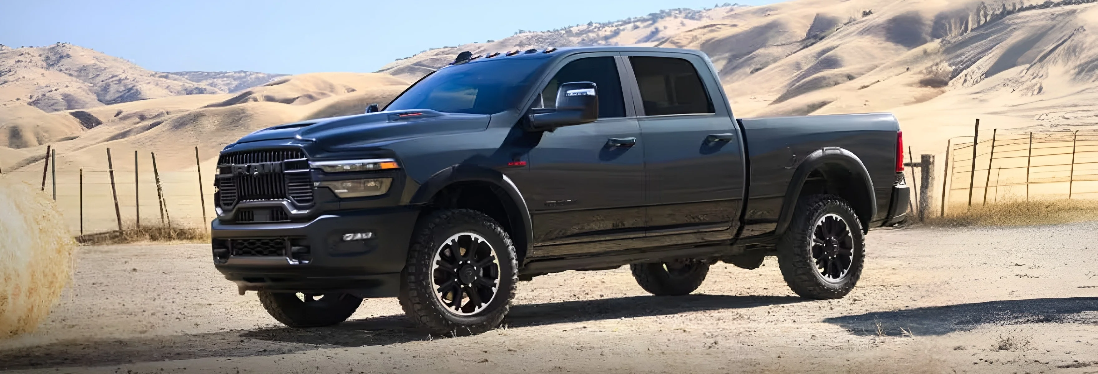 Dark blue RAM 2500 parked in a harvested field with round hay bales and dry hills behind it