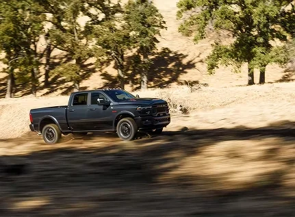 Black RAM 2500 driving along a dirt road past oak trees