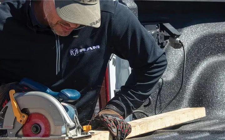 Worker in a RAM jacket cutting a board with a corded circular saw in the bed of a RAM 2500