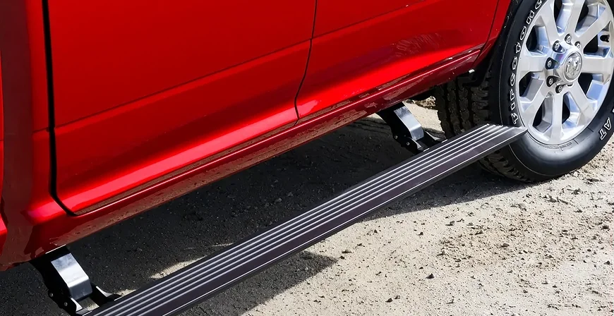 Deployed power side running board along the rocker panel of a red RAM 3500 on gravel
