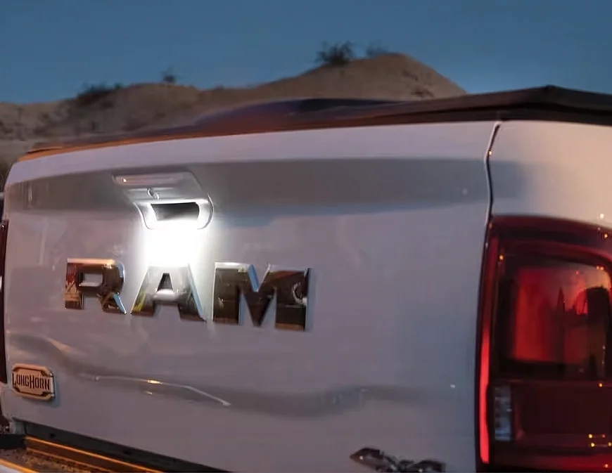 Illuminated RAM tailgate lettering lighting the hitch area of a white RAM 3500 at dusk