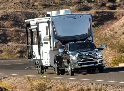Black RAM 3500 towing a large silver fifth-wheel camper around a curve
