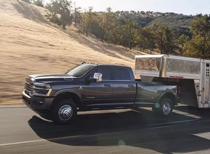 Dark gray dually RAM 3500 towing a livestock trailer on a hillside road