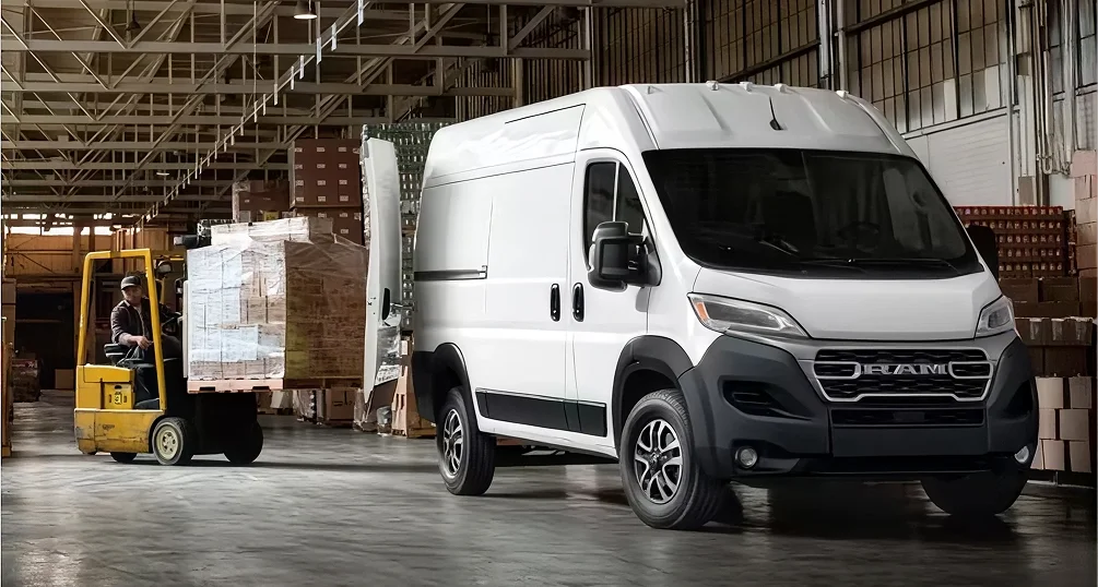 Man using a forklift to load pallets of goods into a white RAM ProMaster cargo van in a warehouse
