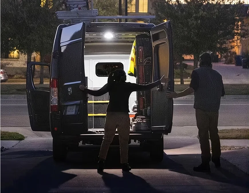 Two people loading a white RAM ProMaster cargo van through its open rear doors at night