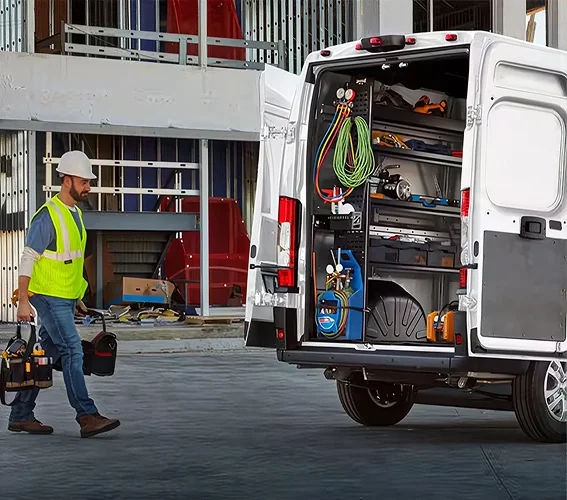 Worker loading tools and equipment into the open side door of a white RAM ProMaster crew van
