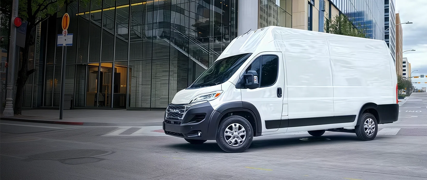 White RAM ProMaster cargo van driving down a city street lined with tall buildings