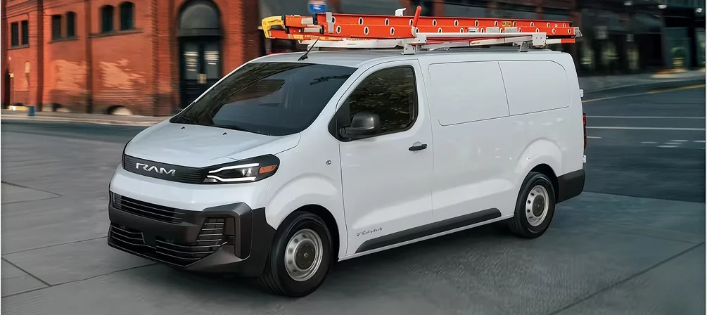 White RAM ProMaster City van with a red ladder on its roof rack driving past a brick building