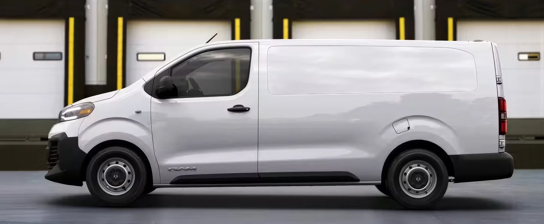 Side profile of a white RAM ProMaster City cargo van in front of a row of yellow-trimmed warehouse bay doors