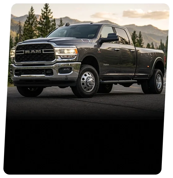 Gray RAM heavy-duty dually pickup on a mountain road lined with pine trees