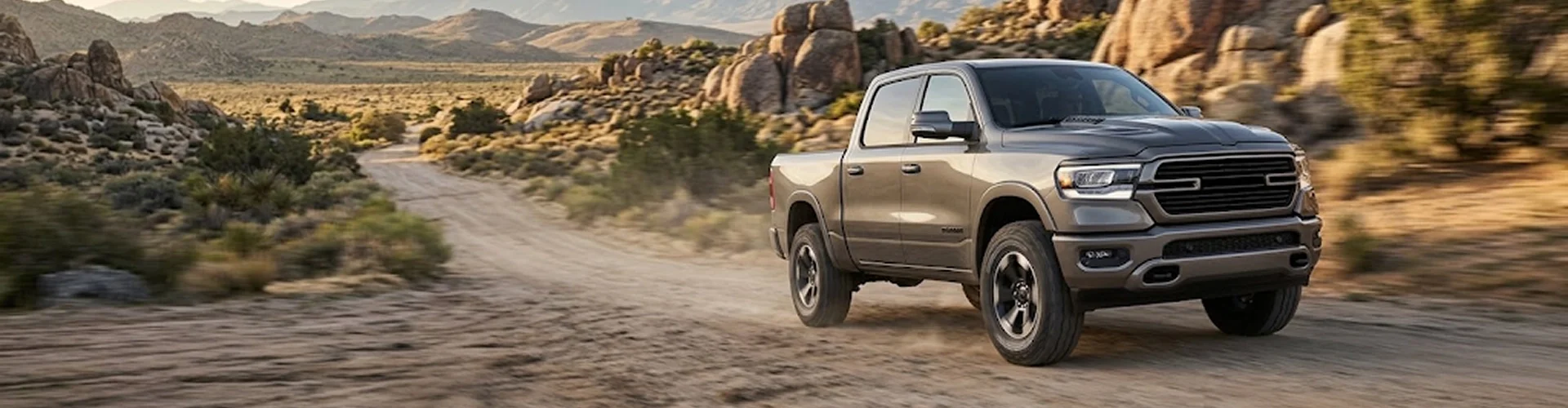 A Ram 1500 driving down a dirt trail through the desert with rock formations and mountains in the distance