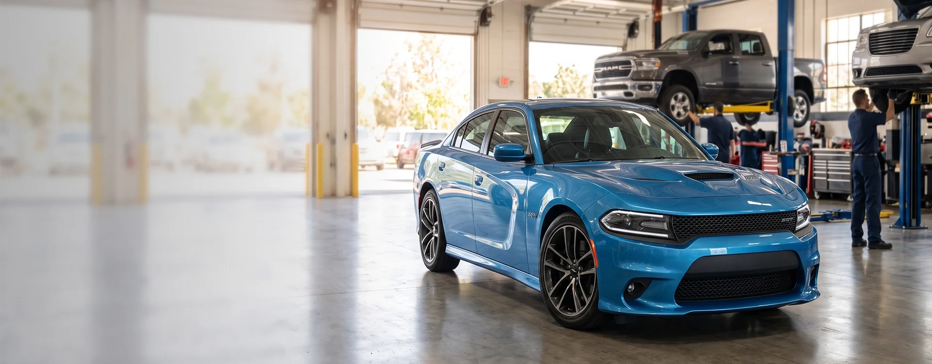A blue Dodge Charger parked inside the Briggs Dodge Ram FIAT service shop with a Ram 1500 and another vehicle raised on lifts behind it