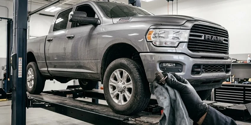 A gloved technician working at the front bumper of a Ram heavy duty pickup parked on a service lift