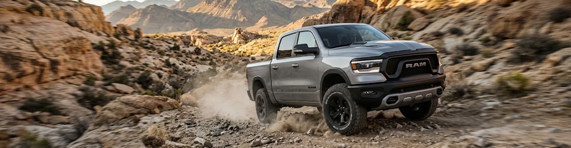 A silver Ram 1500 Rebel climbing a rocky desert trail in four-wheel drive, dust kicking up behind the rear wheels