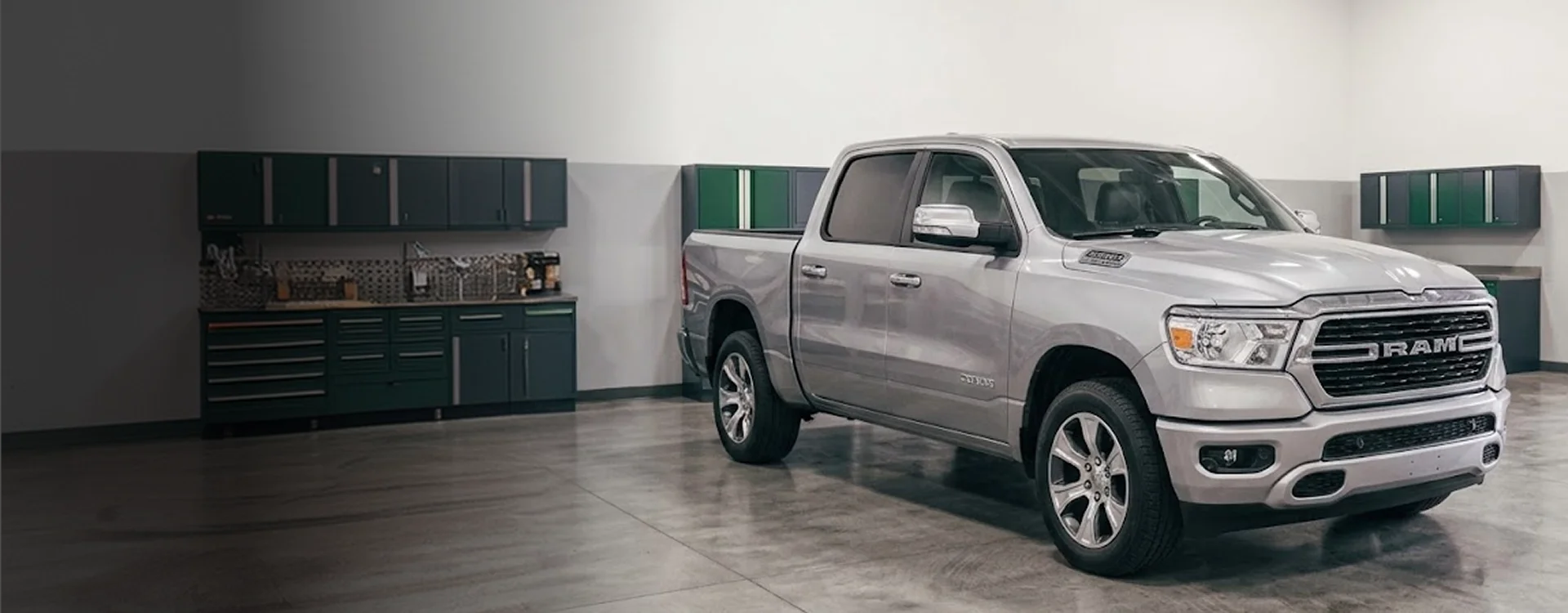 A silver Ram 1500 parked inside a Briggs Dodge Ram Fiat service bay, green cabinets and tool chests lining the wall behind it