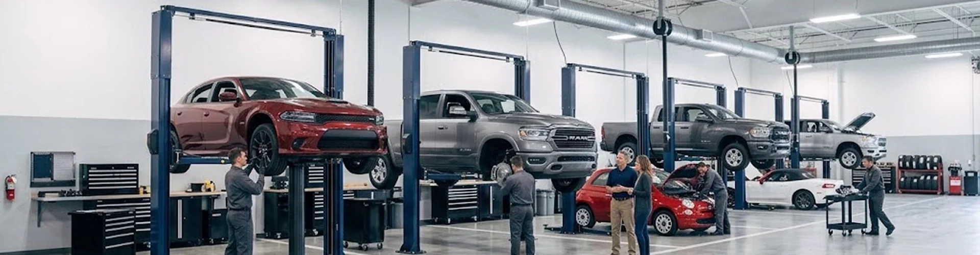 A wide view of the Briggs Dodge Ram Fiat service department with a red Dodge Charger, a grey Ram 1500 and other vehicles raised on lifts while technicians work across the floor