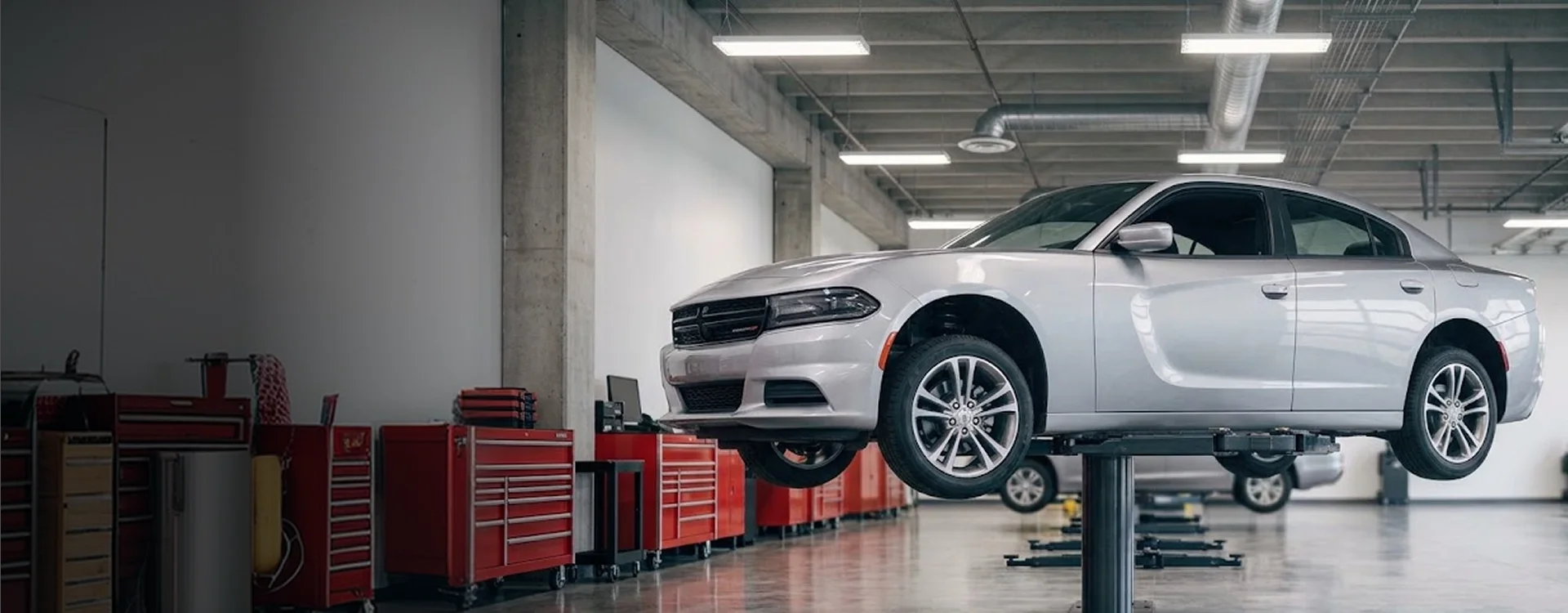 A silver Dodge Charger raised on a service lift inside the Briggs Dodge Ram Fiat shop, red tool chests and further lifts running down the bay behind it