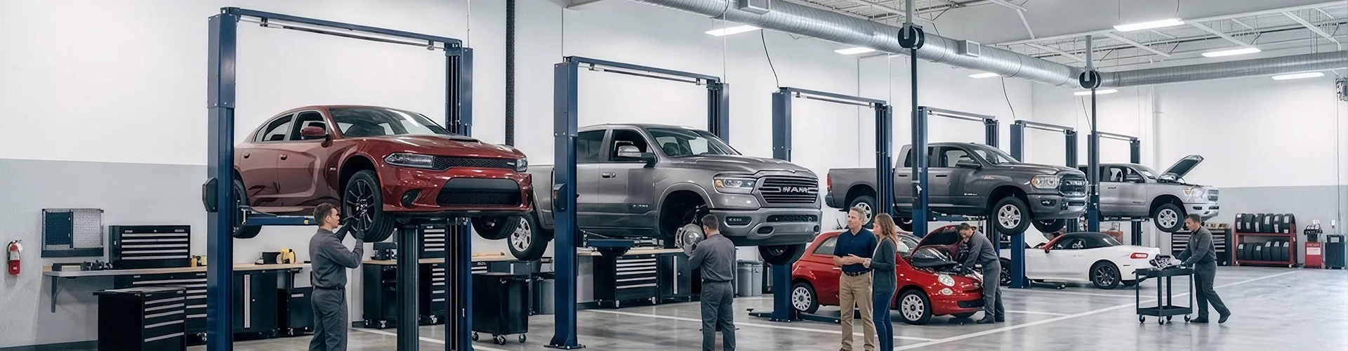 A wide view of the Briggs Dodge Ram Fiat service department with a red Dodge Charger, a grey Ram 1500 and other vehicles raised on lifts while technicians work across the floor